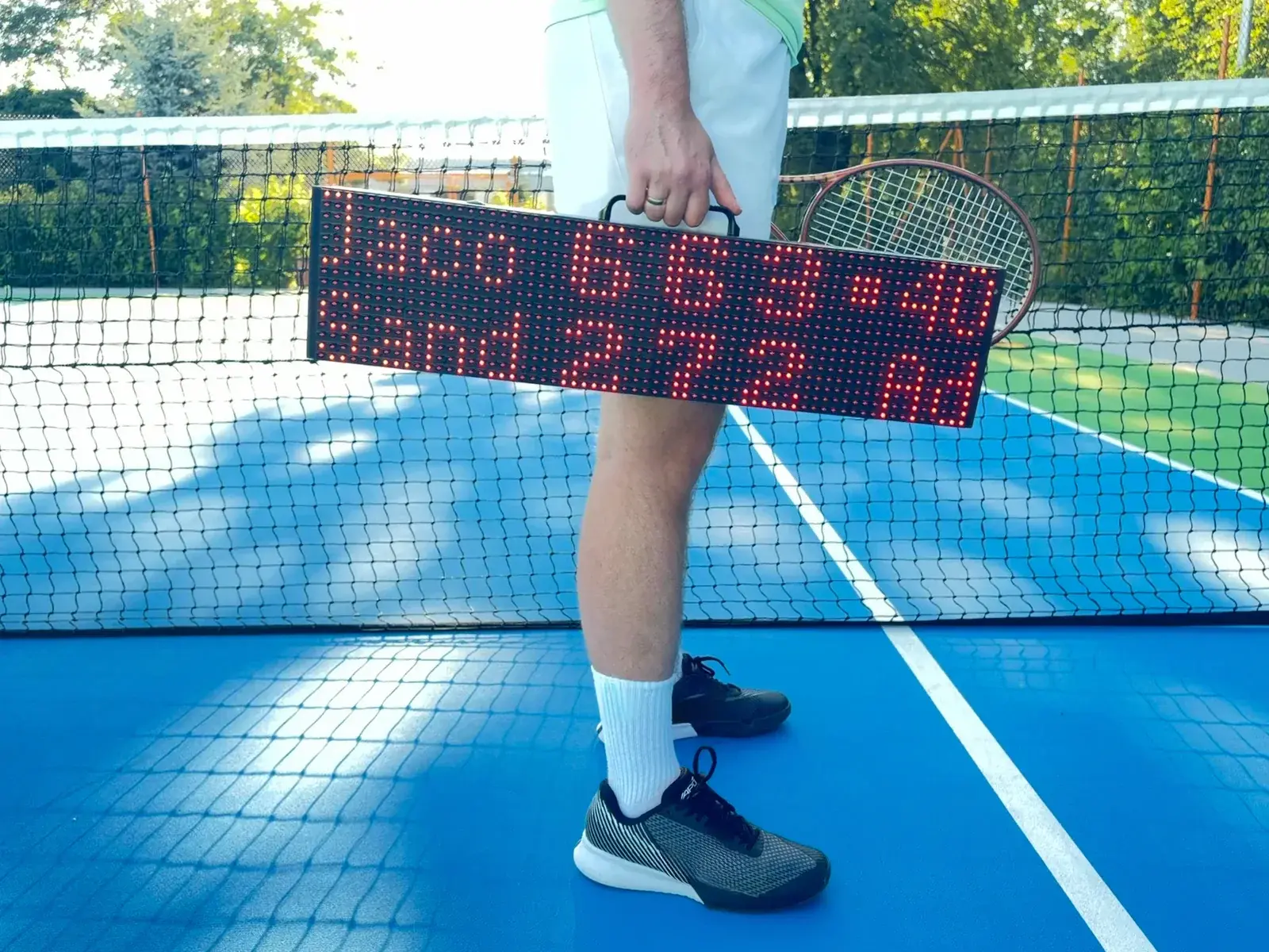 Person carrying the ScreenBattle scoreboard by its integrated handle on a tennis court