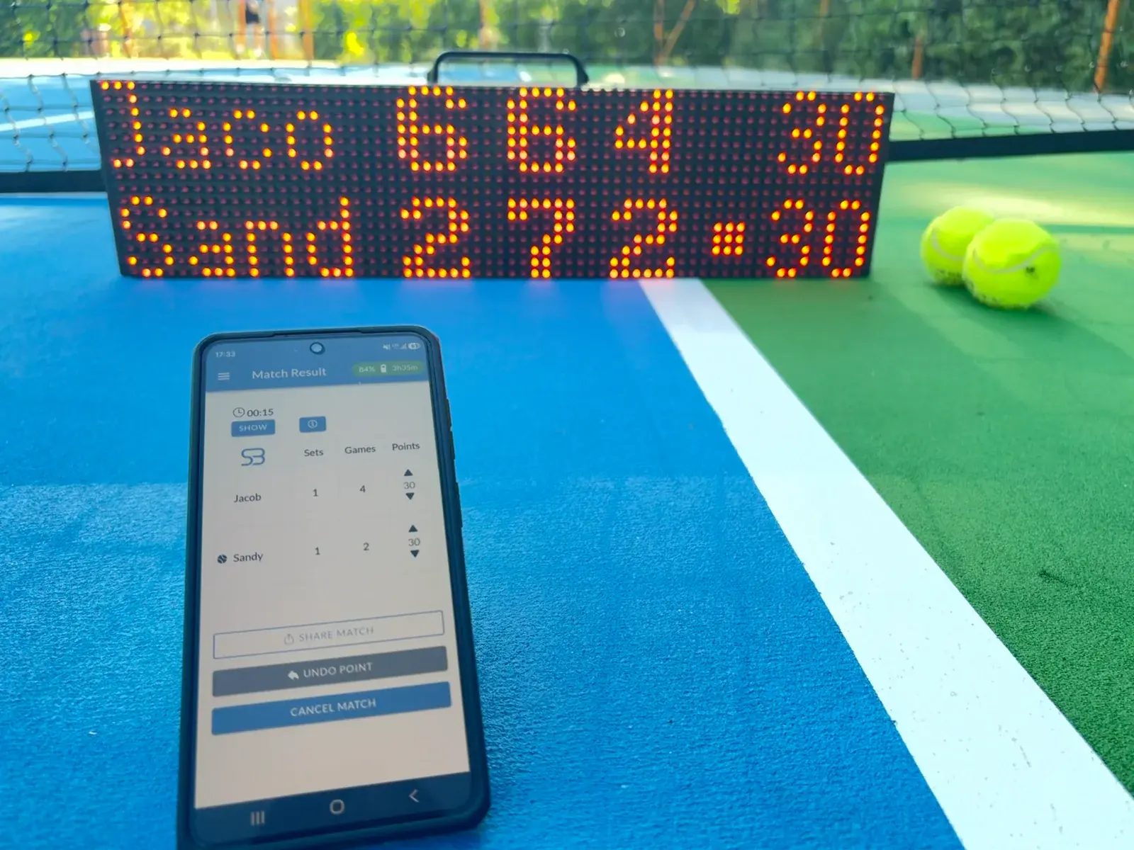 Phone running the ScreenBattle app and controlling the score shown on the LED scoreboard in the background